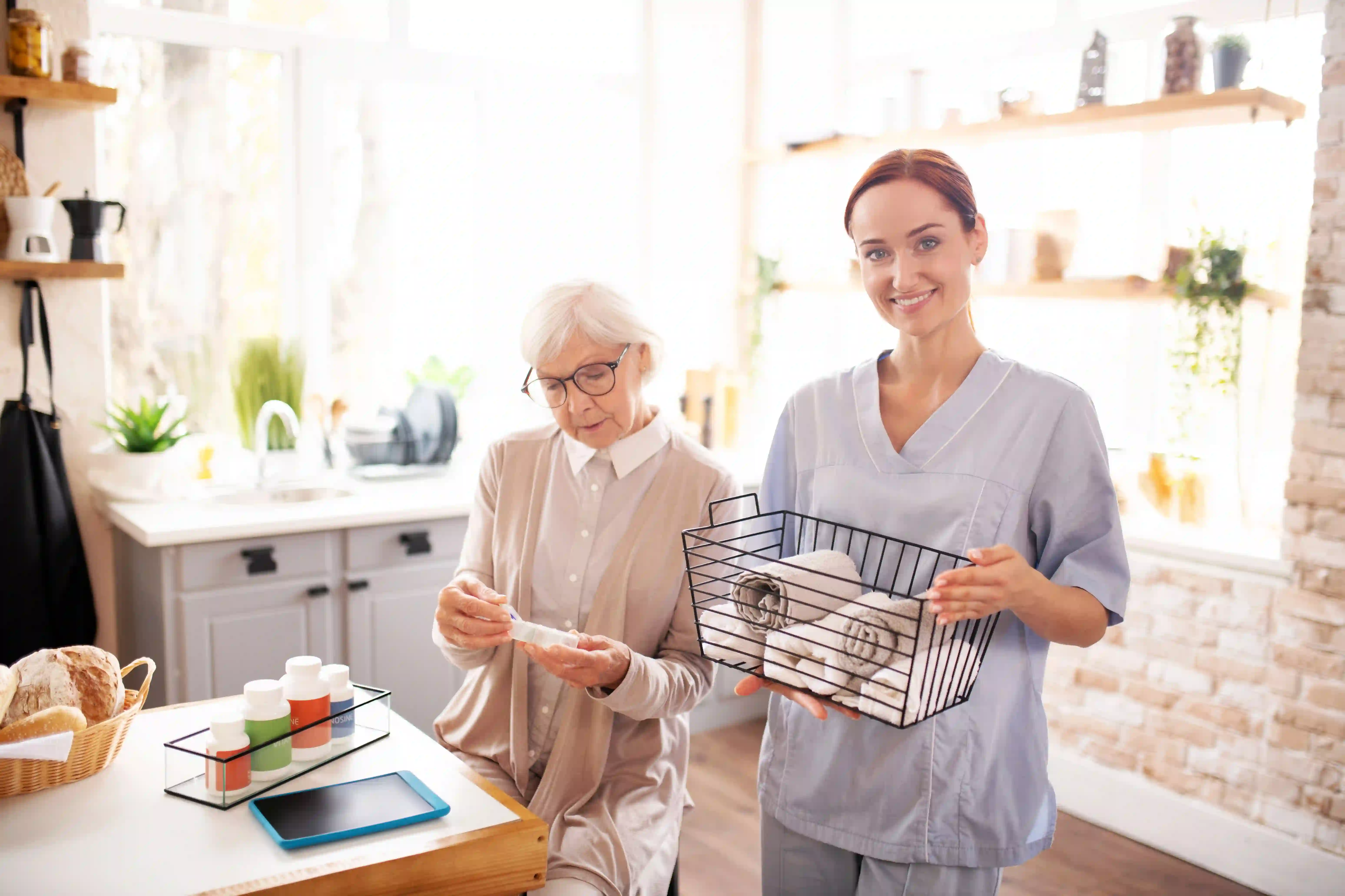 Friendly caregiver helping a senior woman in a sunny group home kitchen